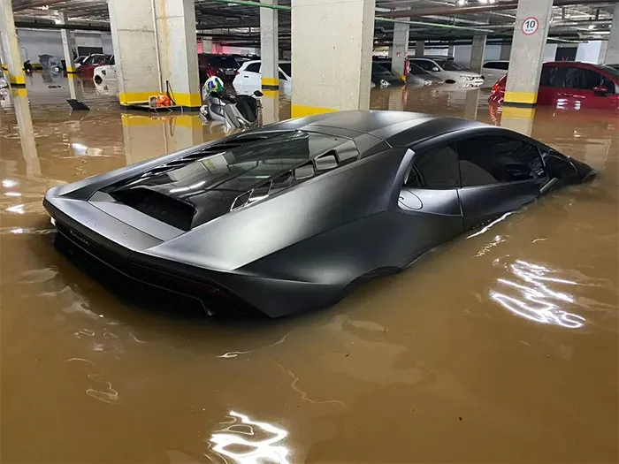 Luxury sports car submerged in muddy floodwater inside a parking garage, showing nature made people go well that sucks.