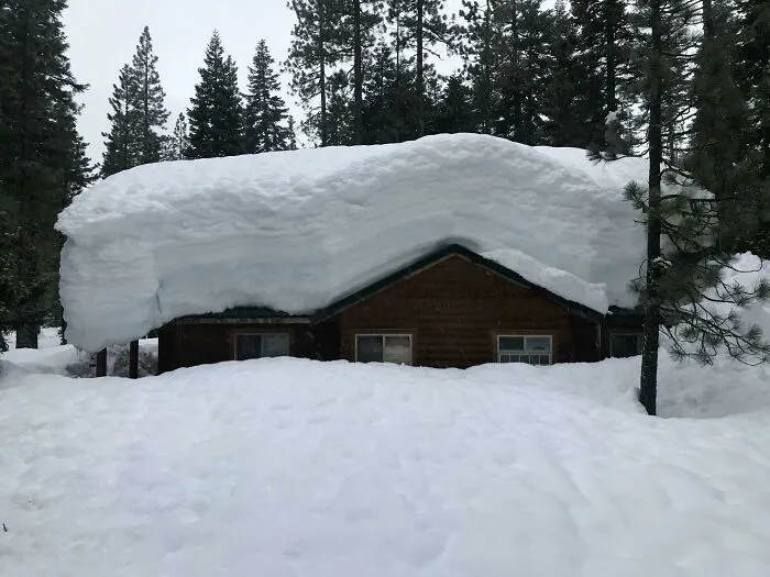 Log cabin buried under an enormous snow load, illustrating nature challenges that make people go well that sucks.