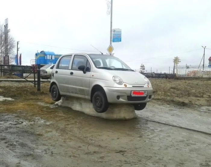 Silver car stuck on a melting ice block in a muddy area, showing a nature moment that made people go well that sucks.