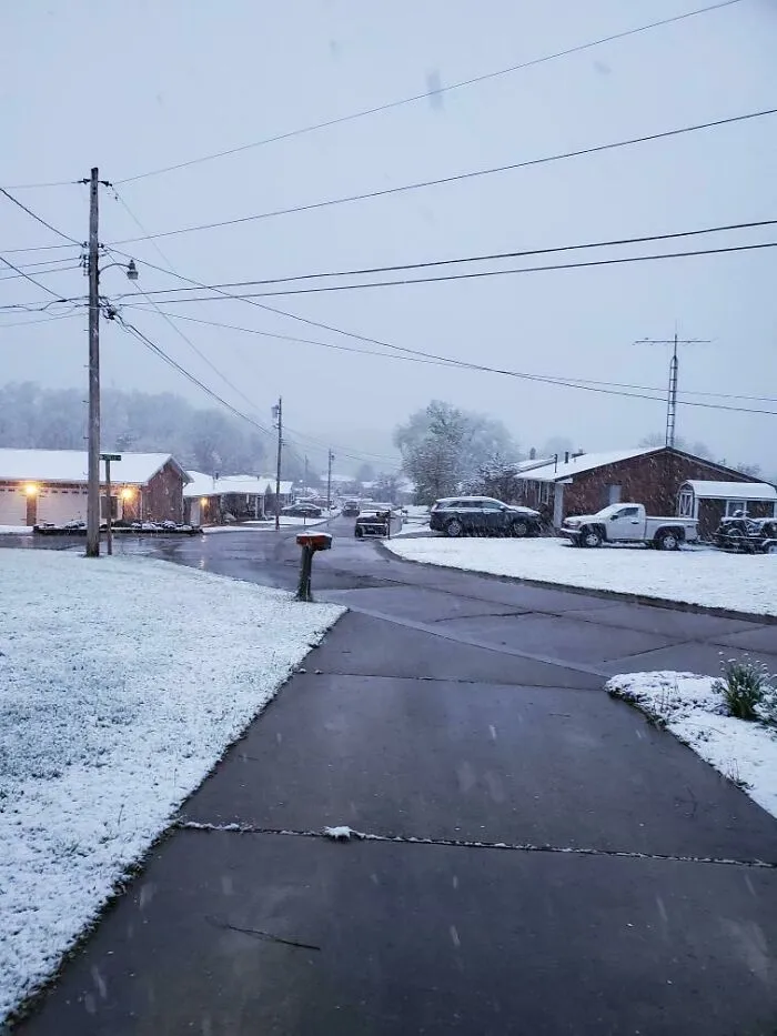 Snow-covered suburban street with cars and houses under a gray sky, showcasing nature made people go well that sucks moments.