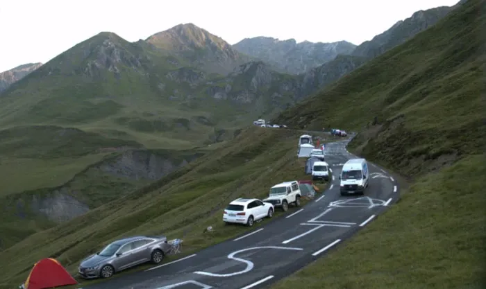 Cars parked along a winding mountain road surrounded by green hills and peaks, showing cool and interesting facts location.