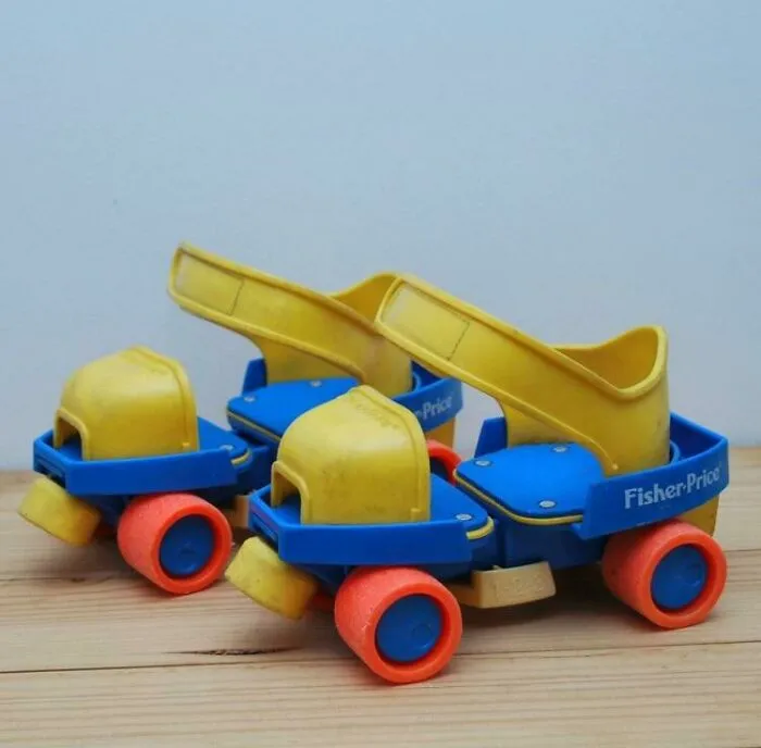 Vintage Fisher-Price roller skates from the '70s era with yellow straps and colorful wheels on a wooden floor.