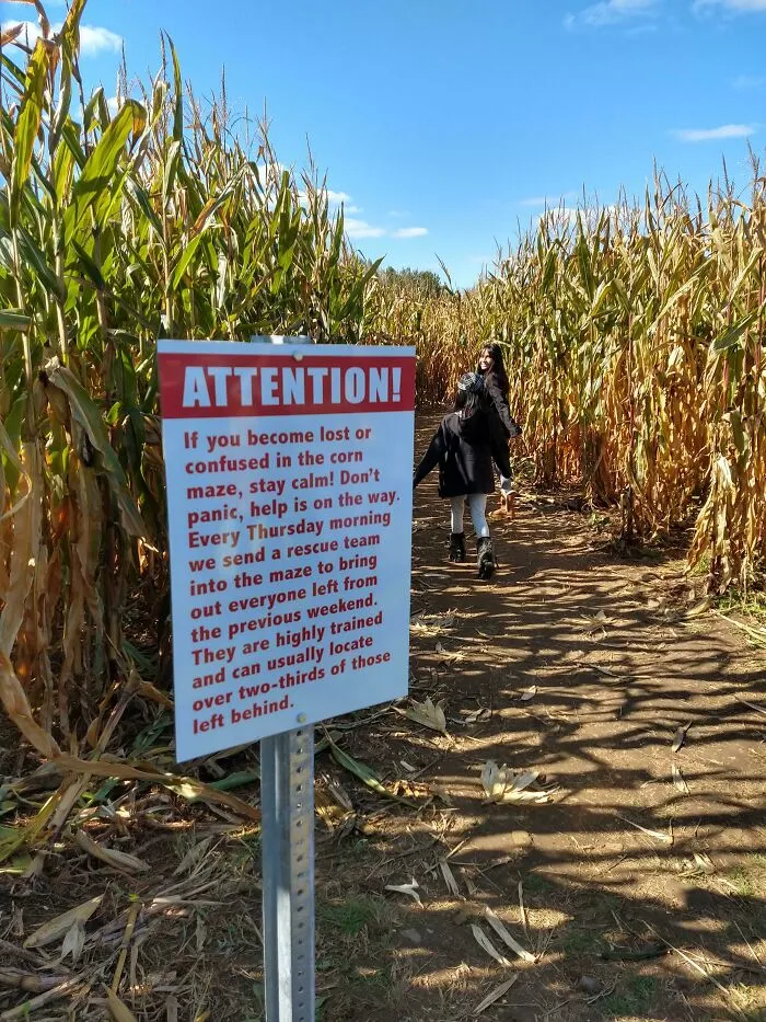 Funny sign in a corn maze warning about getting lost, with people walking ahead.