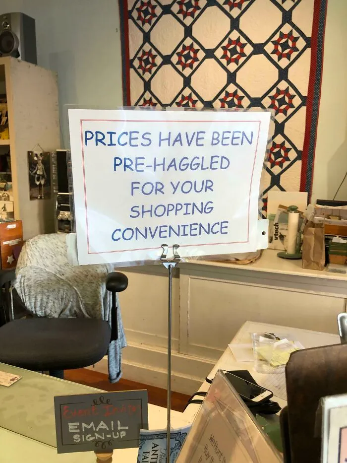 Funny sign in a store reads "Prices have been pre-haggled for your shopping convenience" in a cozy setting.