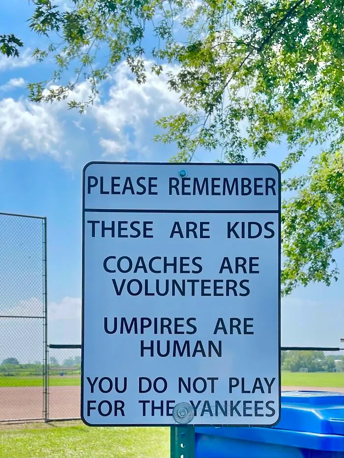 Funny sign at a baseball field reminding spectators that players are kids and umpires are human, with a humorous note about the Yankees.
