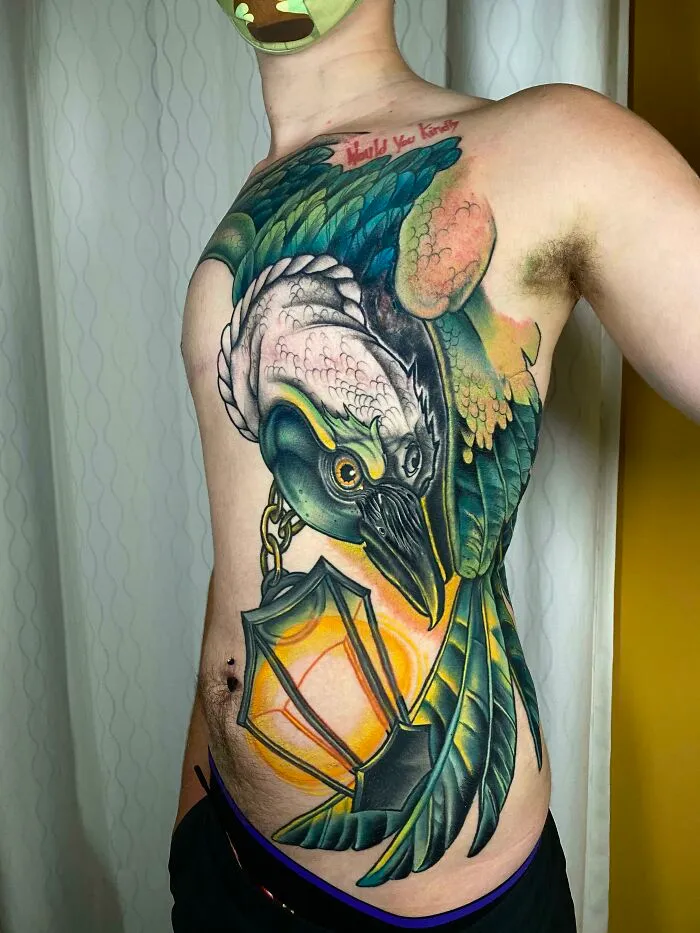 Vibrant tattoo of a bird and lantern creatively covering a birthmark on a person's torso.