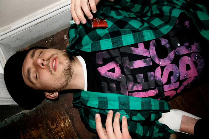 Person lying on the floor wearing a green plaid shirt and graphic tee, related to tattoo virgin experiences.