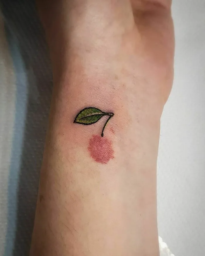 Tattoo of a cherry with a green leaf on a wrist, creatively covering a birthmark.