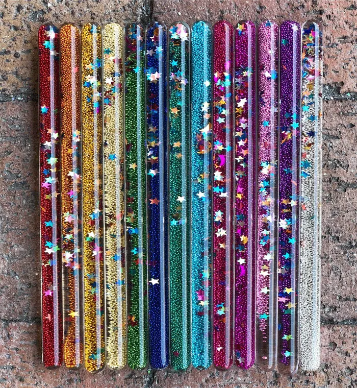 Colorful glitter wands with stars on a brick background, reminiscent of classic toys from the '70s, '80s, and '90s.