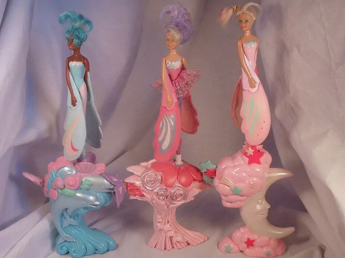 Three vintage toys from the '70s, '80s, and '90s with colorful bases and pastel dresses.