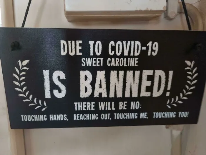 Funny sign about banning "Sweet Caroline" due to COVID-19 with humorous lyrics reference.