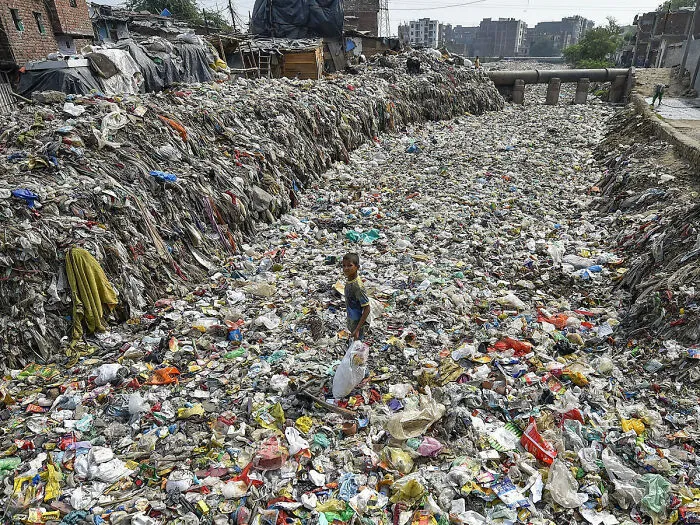A Boy Gathers Recyclable Items From A Semi-Dry Drain, At Taimoor Nagar In New Delhi