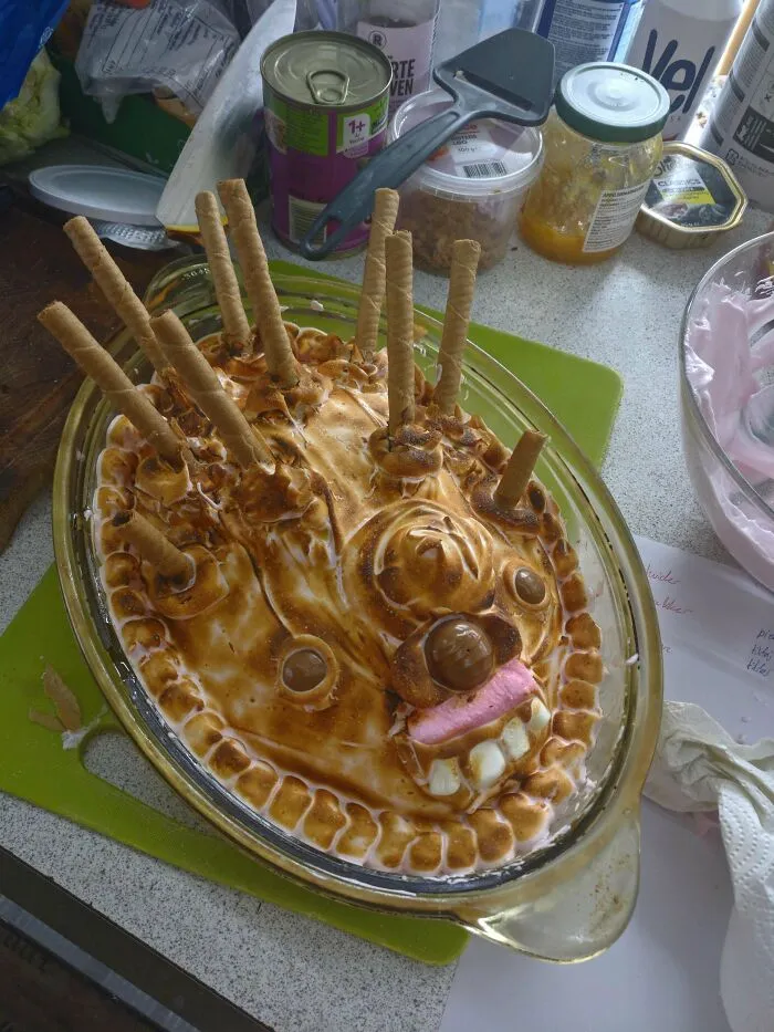 A cake fail featuring a toasted dessert with wafer sticks, candy eyes, and a pink and white marshmallow mouth.