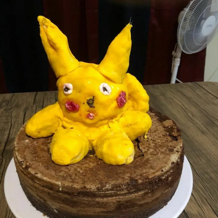 Funny cake fail featuring a poorly crafted yellow character with crooked eyes and ears on a chocolate base.