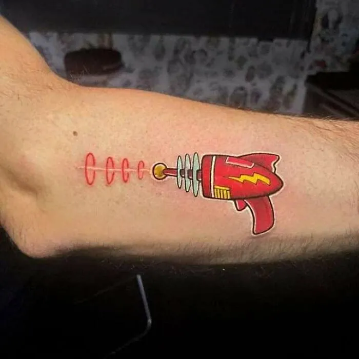 Colorful ray gun tattoo on forearm cleverly covers a scar, showcasing creative cover-up art.