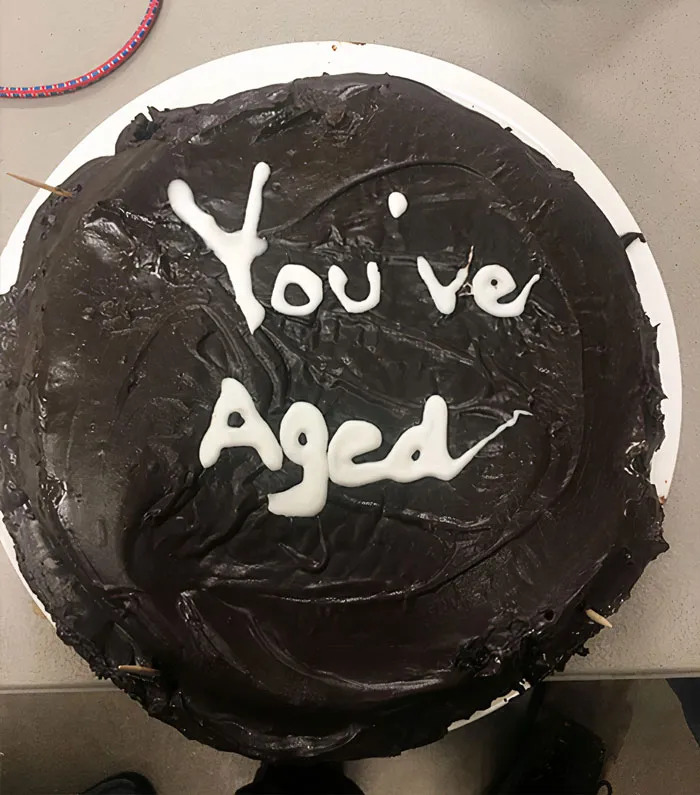 Chocolate cake with uneven icing reading "You've Aged," a humorous cake fail.