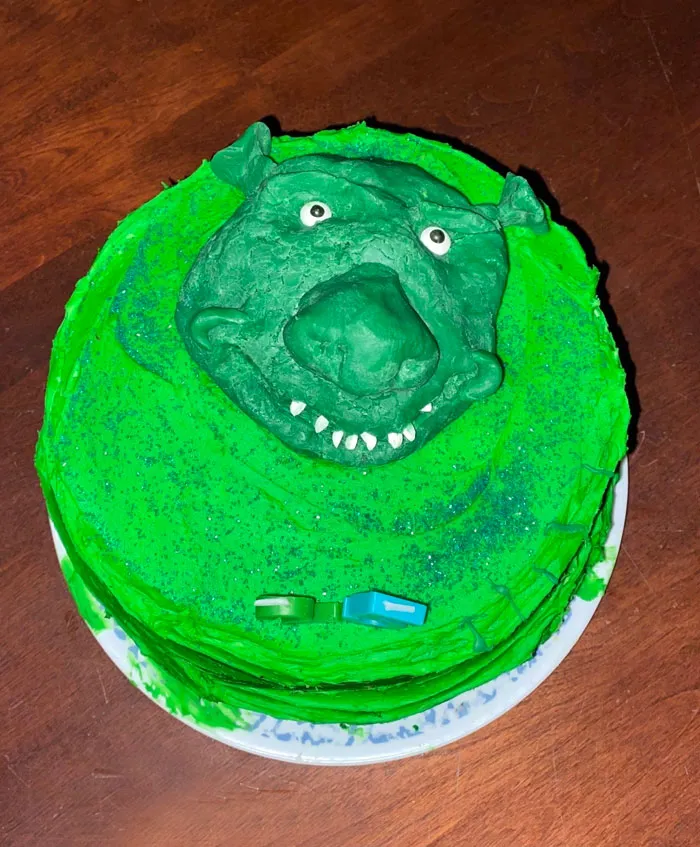 Funny cake fail with a misshapen green Shrek-like face on top, showcasing a humorous decoration attempt.