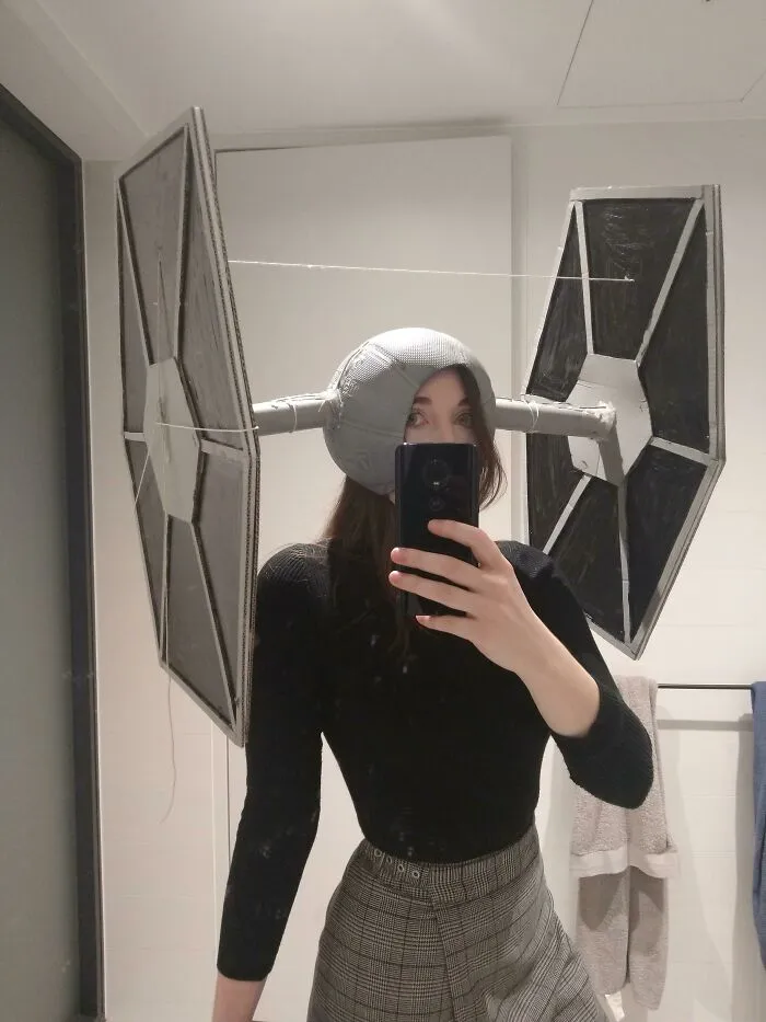 Person wearing a creative Halloween costume with large homemade starfighter wings made from cardboard and tape.