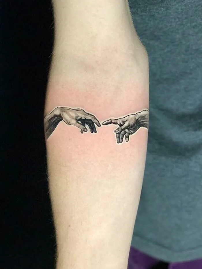 Tattoo of two hands reaching towards each other on a person's forearm, inspired by intricate first tattoo ideas.