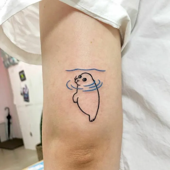 Seal tattoo on arm, showcasing an interesting first tattoo idea with simple lines and blue water accents.