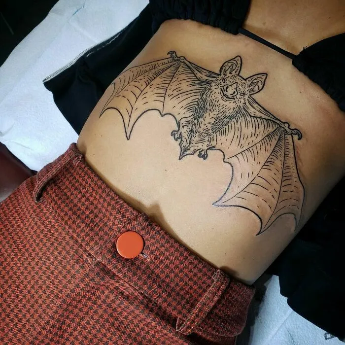 Bat tattoo on person's stomach, showcasing spooky Halloween design for horror lovers.