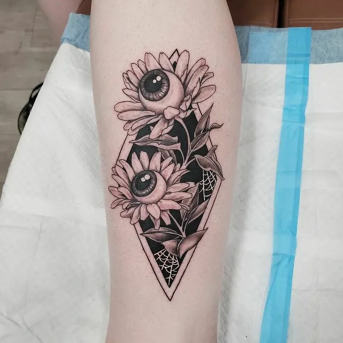 Spooky Halloween tattoo of sunflowers with eyeballs on arm, showcasing creative horror-inspired ink art.