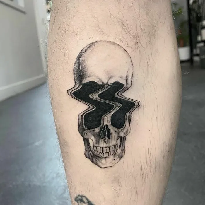 Spooky Halloween tattoo of a skull with distorted eye sockets on a person's leg.