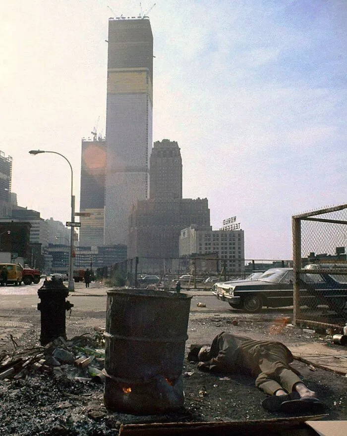 Un indigente duerme junto a un bote de 50 galones con madera en llamas frente al World Trade Center en construcción, Nueva York, 1970