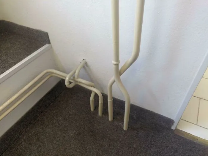 Awful home interior with awkwardly arranged pipes near a staircase.
