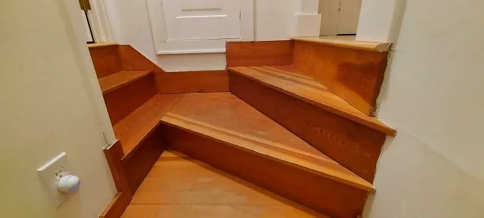 Awful interior design with awkwardly angled wooden stairs in a narrow hallway.