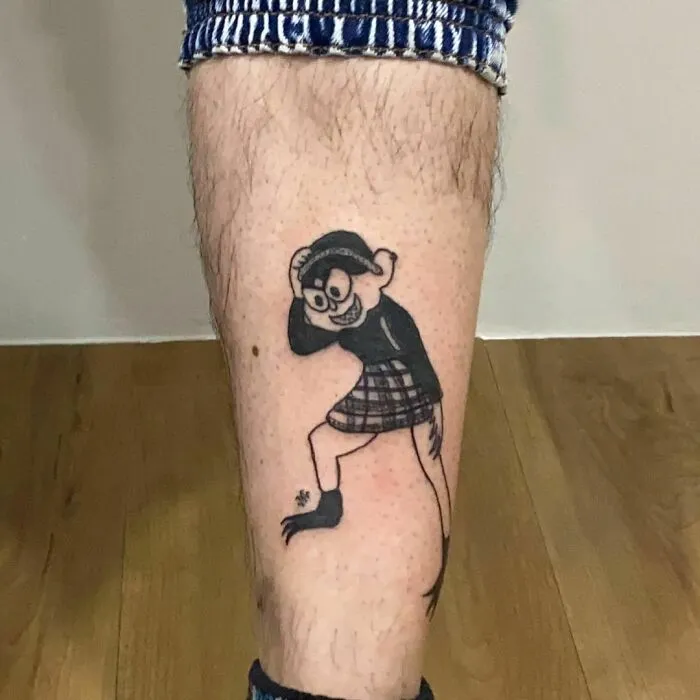 Tattoo of a quirky character in plaid on a leg, showcasing unique design by a popular tattoo artist known for her style.