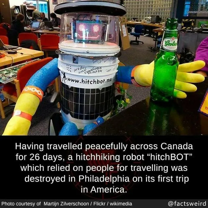 Hitchhiking robot hitchBOT with LED face and colorful arms holding a beer bottle, illustrating weird facts about the world.