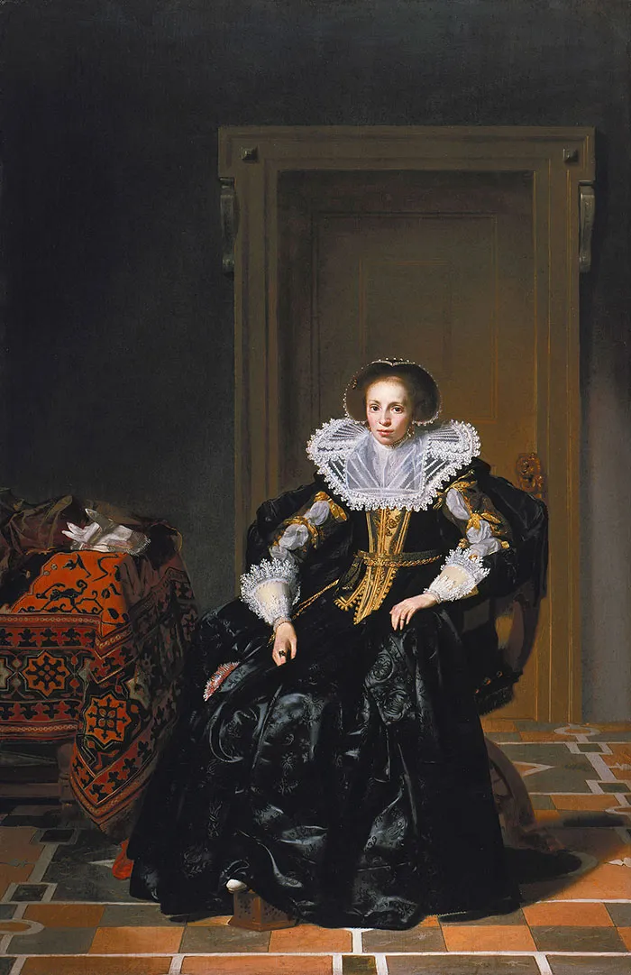 A woman in elaborate 17th-century dress seated indoors, representing famous paintings in art history.
