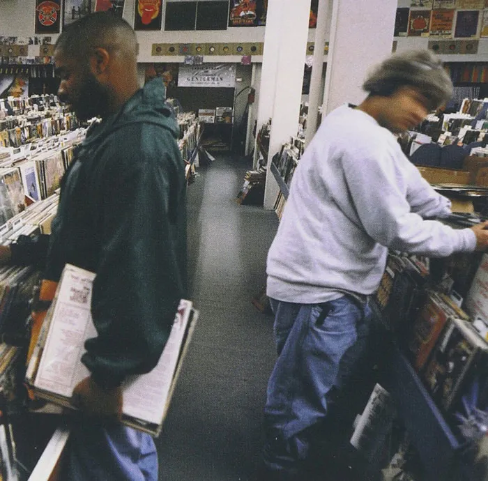 Two people browsing vinyl records, surrounded by racks of the greatest album covers in a music store.