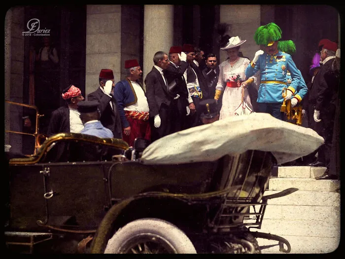 Dressed in period attire, a group stands by a vintage car, capturing an important historical moment.