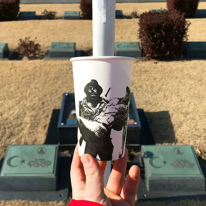 Hand holding a paper cup with black ink illustration, part of artist’s travel drawings featured in cup illustrations series.