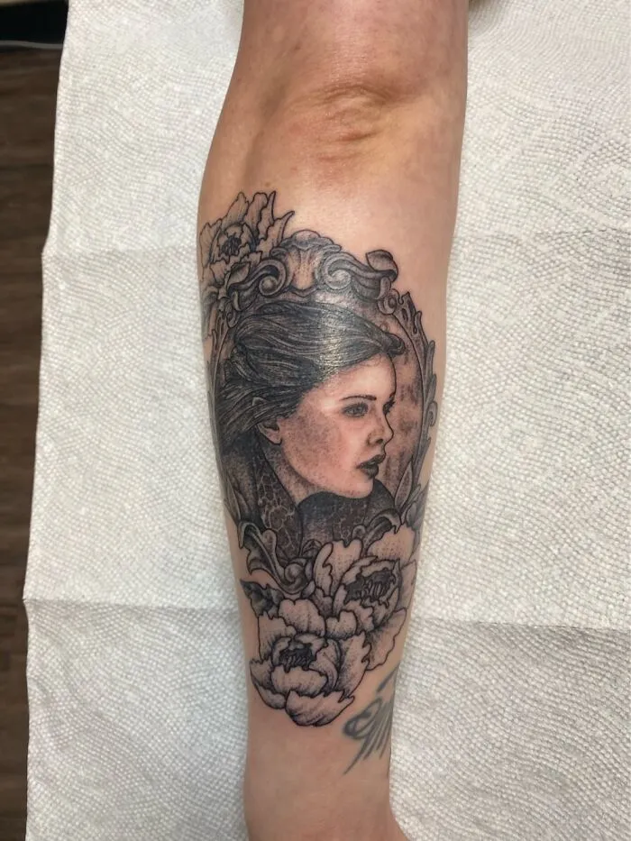 A realistic portrait tattoo with floral details on an arm, showcasing impressive new artwork.