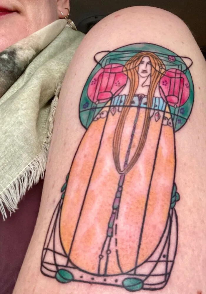 Art Nouveau inspired tattoo of a woman with long hair, featuring vibrant colors and geometric patterns on an arm.