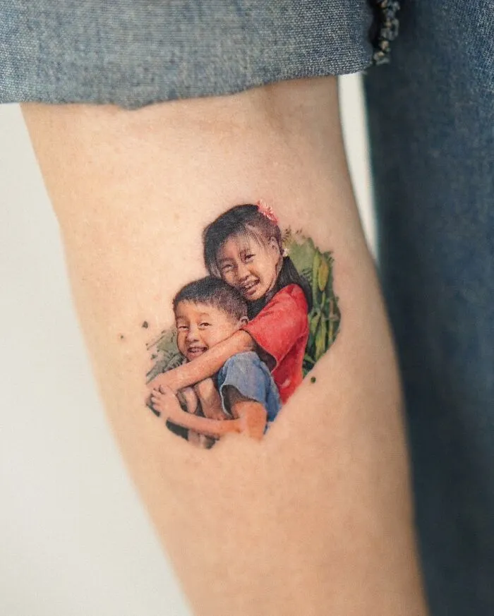 Painting-like tattoo of two smiling children hugging, showcasing artist's skill.