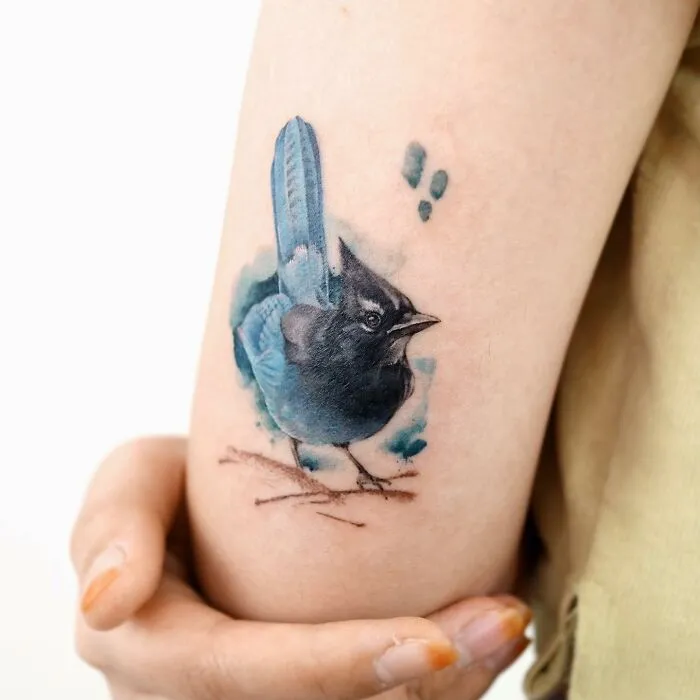 A bird tattoo painted in a realistic style on an arm, showcasing the artist's painting-like tattoo technique.