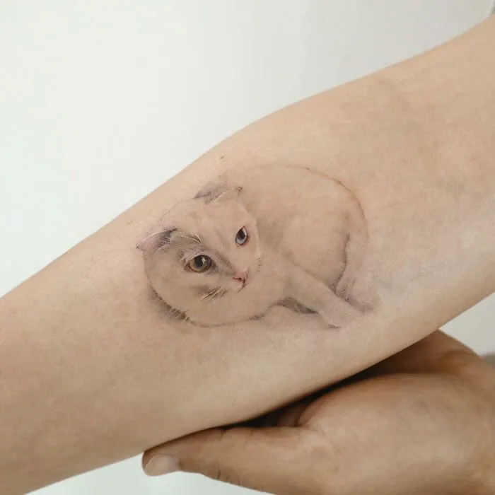 Painting-like tattoo of a realistic cat on a person's arm.