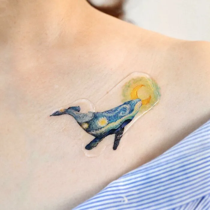 Painting-like tattoo of a whale on a shoulder, featuring vivid colors and artistic details.