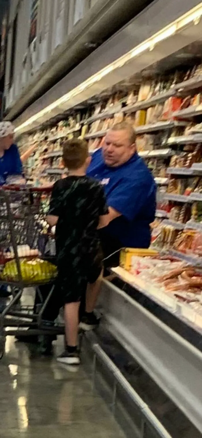 Man sitting in a meat isle talking to a boy 
