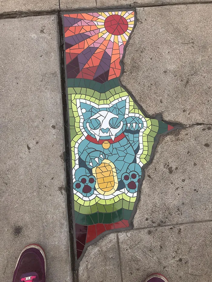 Esta grieta en el pavimento rellenada con un retrato de un gato en mosaico