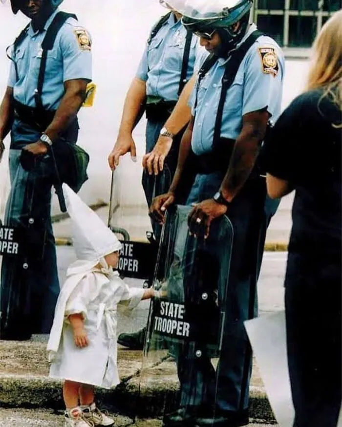 Fotografía de Todd Robertson: "Nadie nace racista". Un niño vestido con una túnica y una capucha del KKK, toca curiosamente el escudo de un policía estatal durante un mitin del KKK en Gainesville, Georgia, 1992