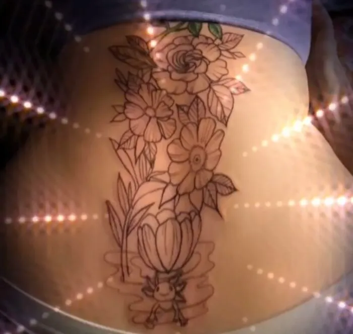 Flower tattoo design on lower back, featuring various blooms and a small character at the base.