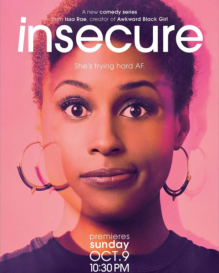 Issa Rae promoting her HBO TV series Insecure, wearing large hoop earrings against a pink background.
