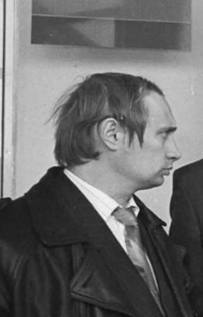 A man wearing a leather coat and tie with an unusual, messy hairstyle in a black and white photo.