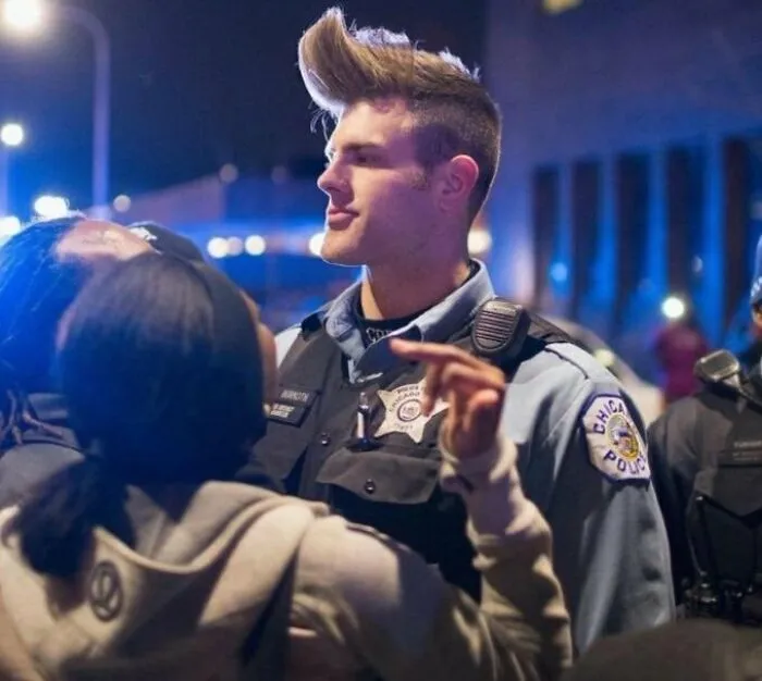Police officer with a dramatic hairstyle during a night event, engaging with the crowd.