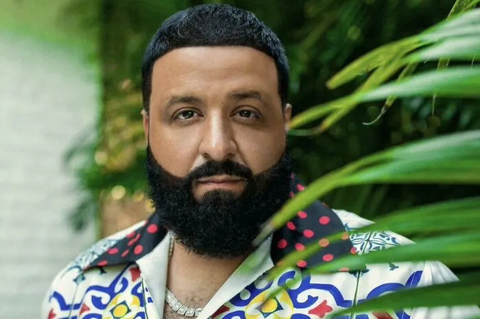 Man with a bold hairstyle and beard, wearing a colorful shirt, surrounded by lush greenery.